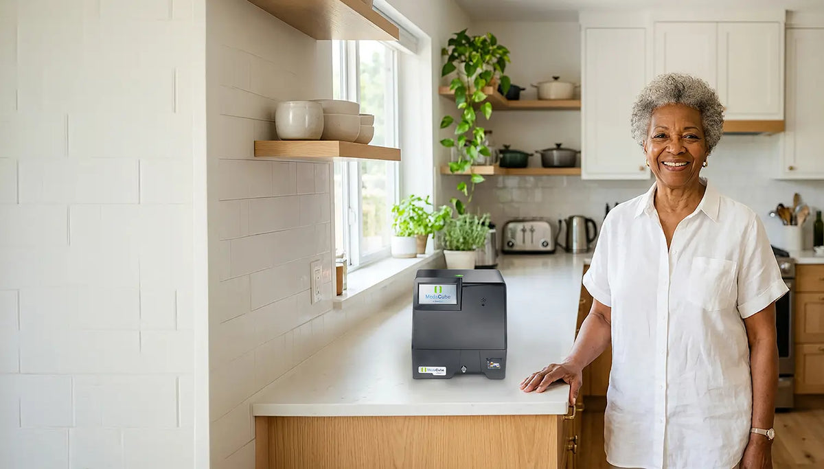 An Older woman standing in her kitchen and smiling next to the MedaCube Automatic Pill Dispenser