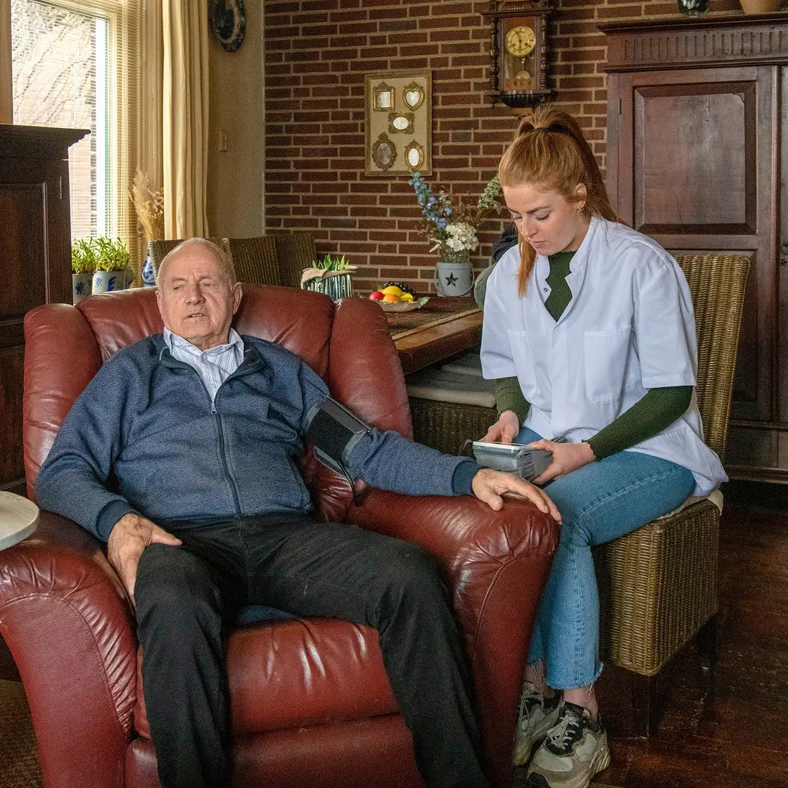 Senior Veteran On Armchair With Caregiver Next To Him
